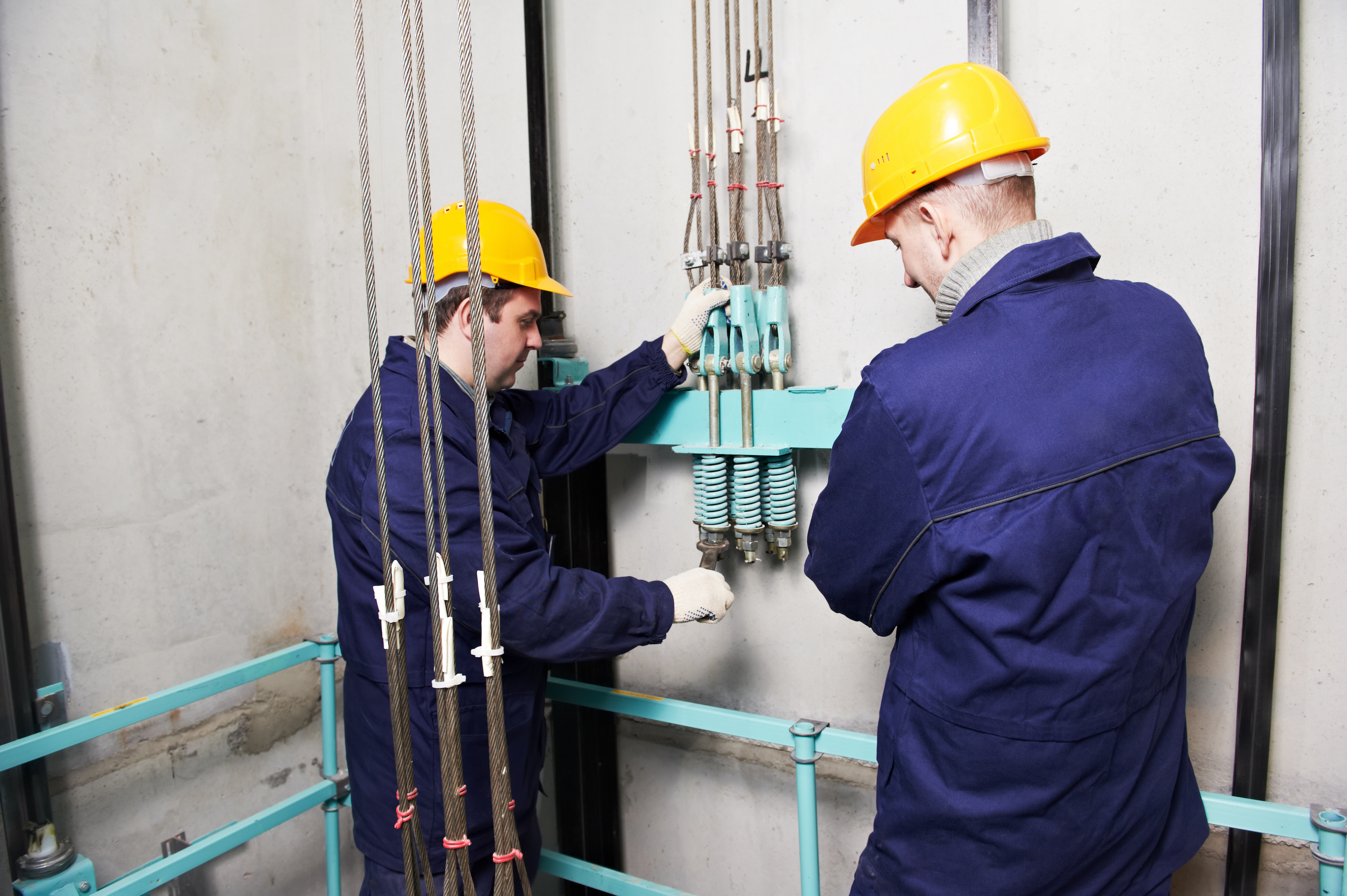 two machinist worker technicians at work adjusting lift with spanners in elevator hoistway